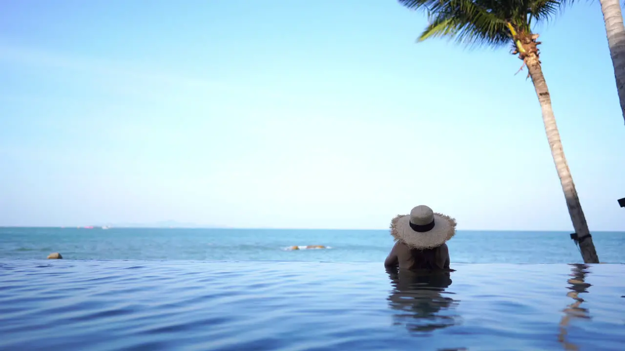 A woman relaxing in an infinity swimming pool during the day looking out at the ocean view