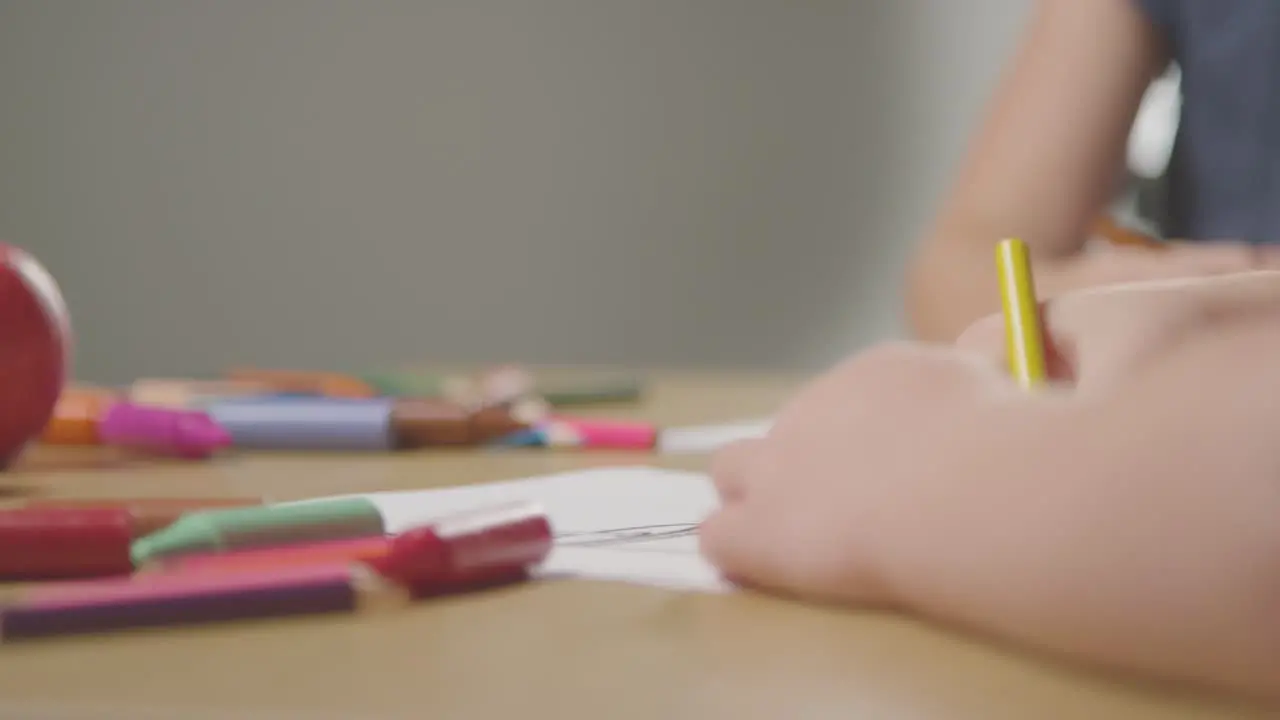 Close Up Of Two Children At Home Drawing And Colouring In Pictures At Table