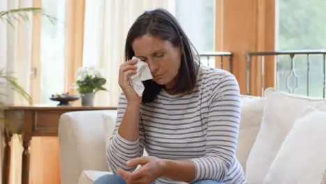 Wide Shot of Visibly Upset Middle Aged Woman Dabbing Eye with Tissue