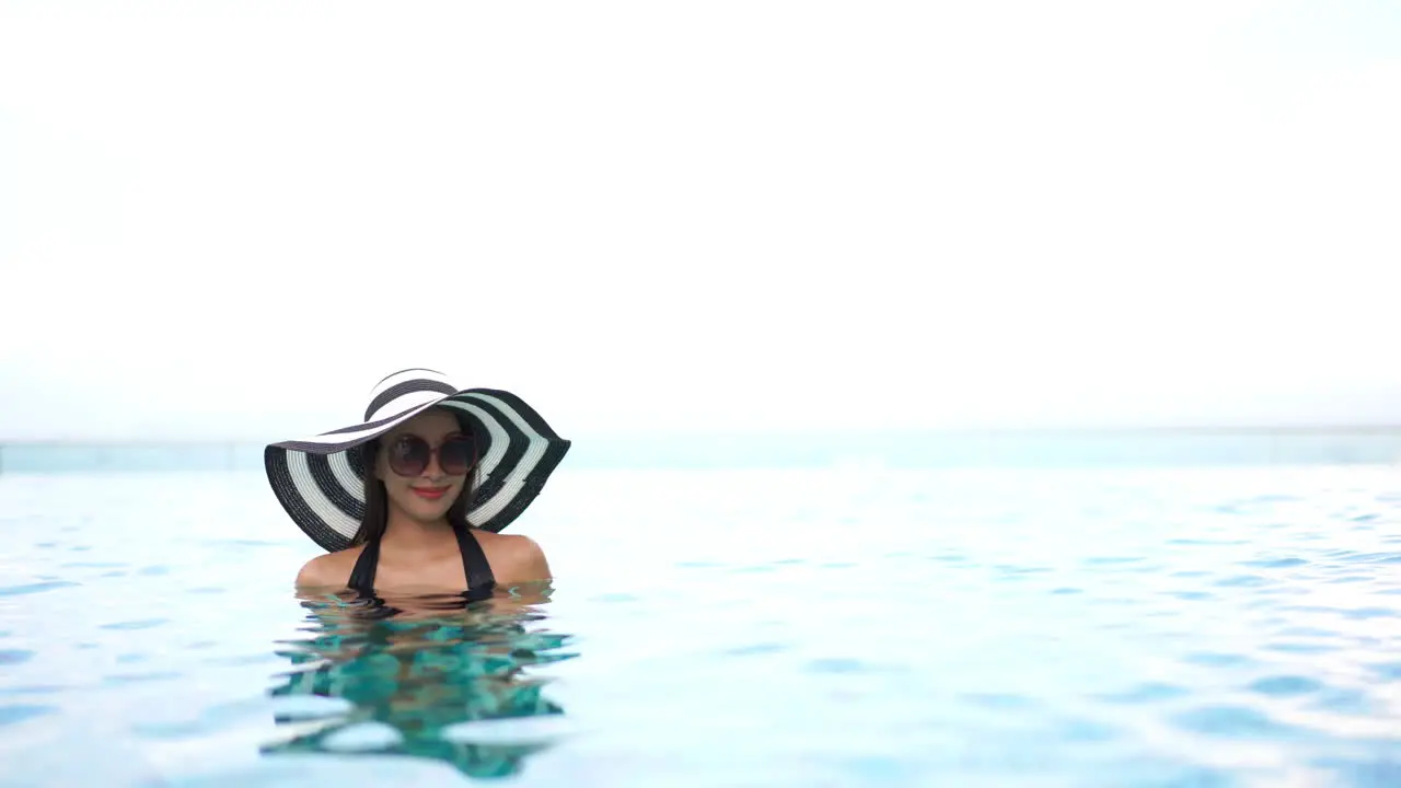 smiling woman surrounded by crystal blue rippling water and bright sunlight wearing a striped hat and sunglasses