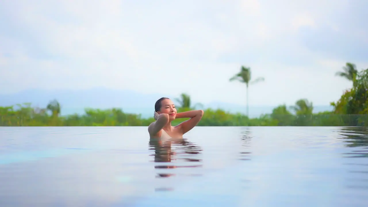 Exotic Woman on Tropical Destination Enjoying in Pool With Green Landscape in Background Fixing Wet Hair Slow Motion