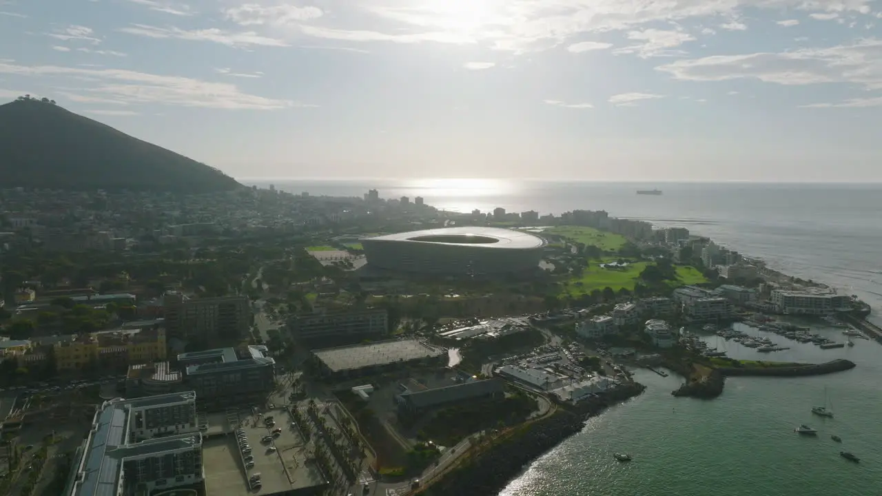 Aerial view of sea coast and buildings on waterfront Modern circular structure of football stadium against setting sun Cape Town South Africa