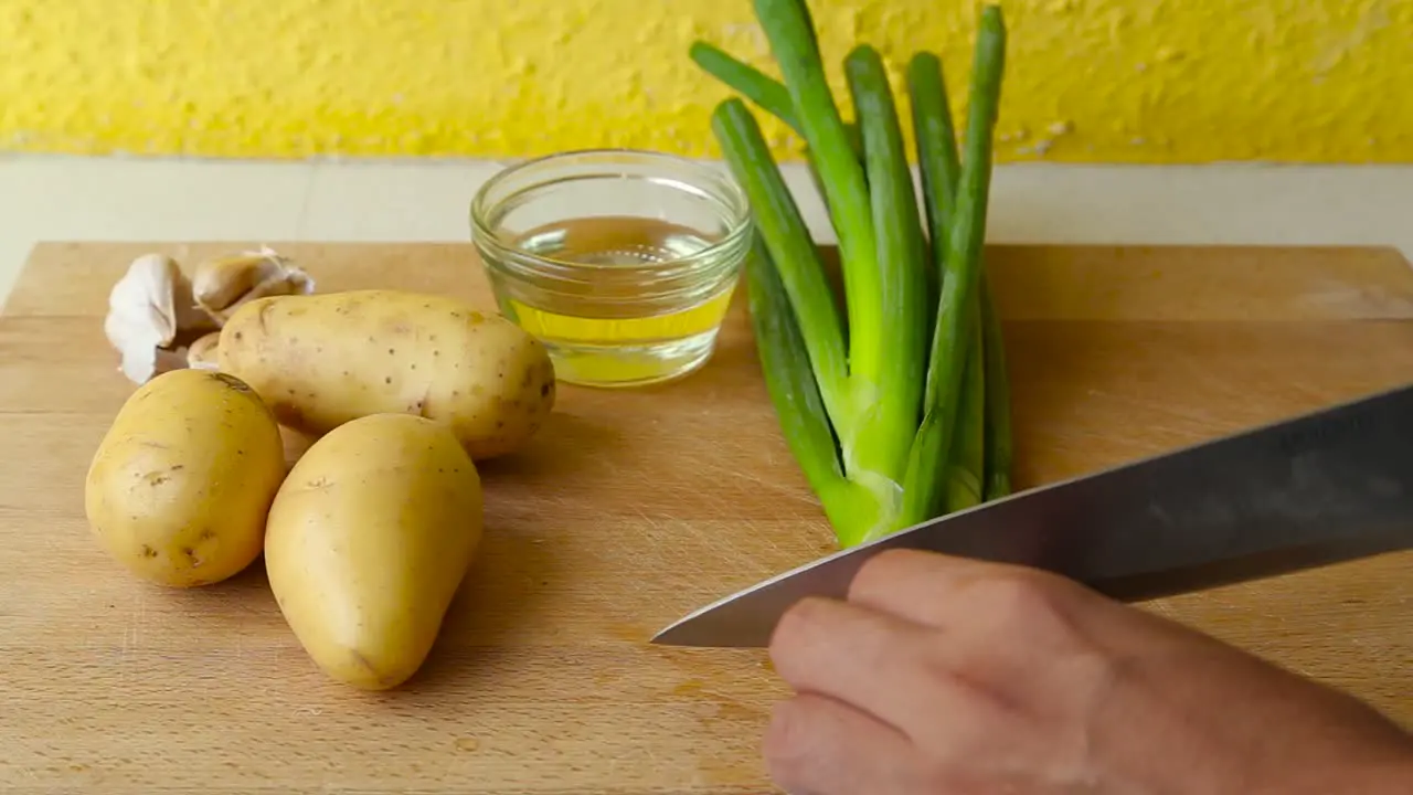 Male hand cutting green onion on wooden cutting board