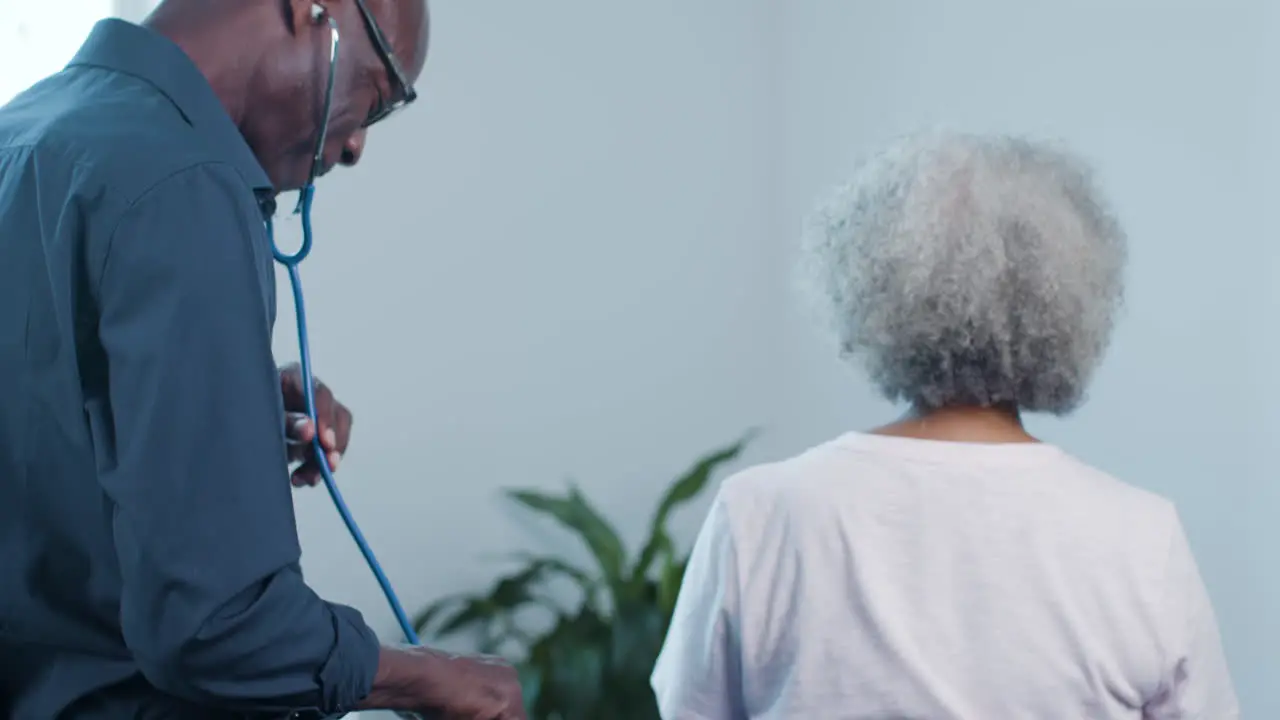 Middle Aged Male Doctor Uses Stethoscope On Patient's Back