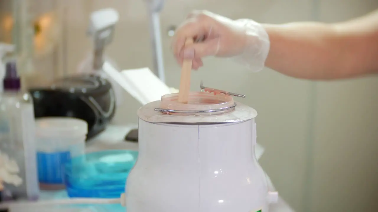 A beautitian prepares for leg waxing by applying wax to a spatula from a xax pot