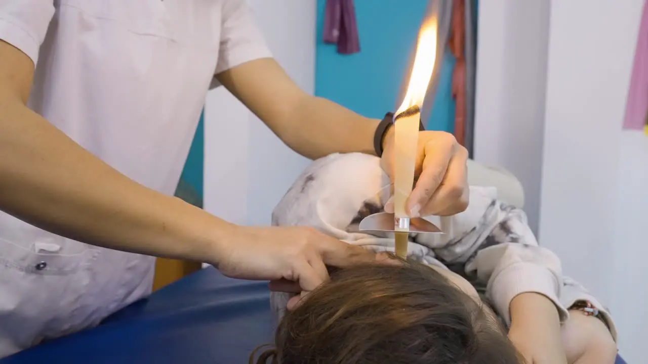 Close-up of a therapist performing an ear wax removal treatment on a patient using candling