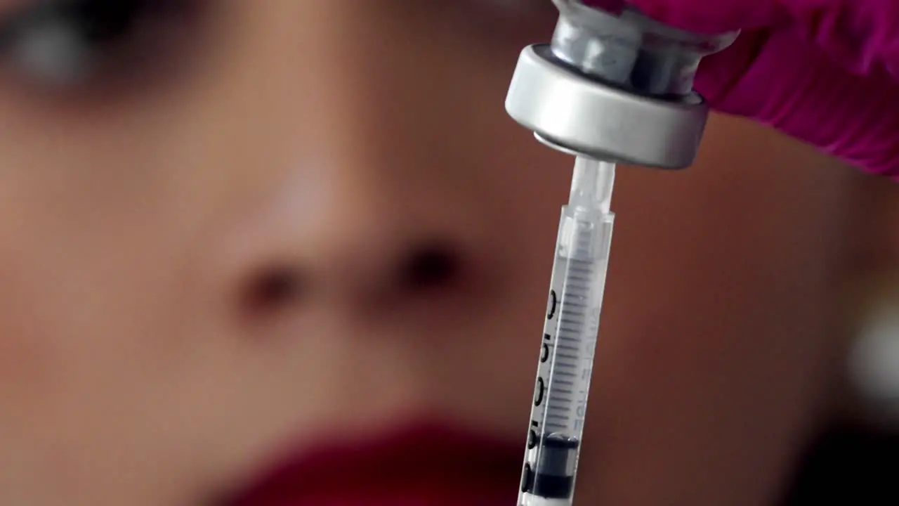 Female doctor or nurse fills a syringe from a vial of medication close up