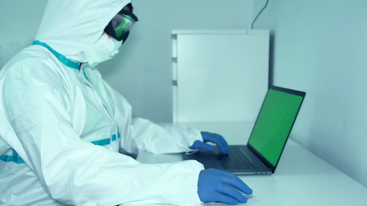 Healthcare Worker In Full PPE Working On The Laptop For Research During Pandemic- medium shot