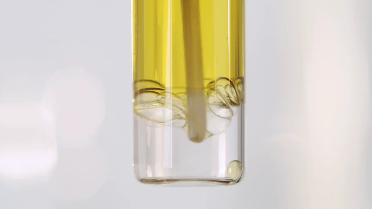 A container of yellow oily liquid being stirred with a bright white background