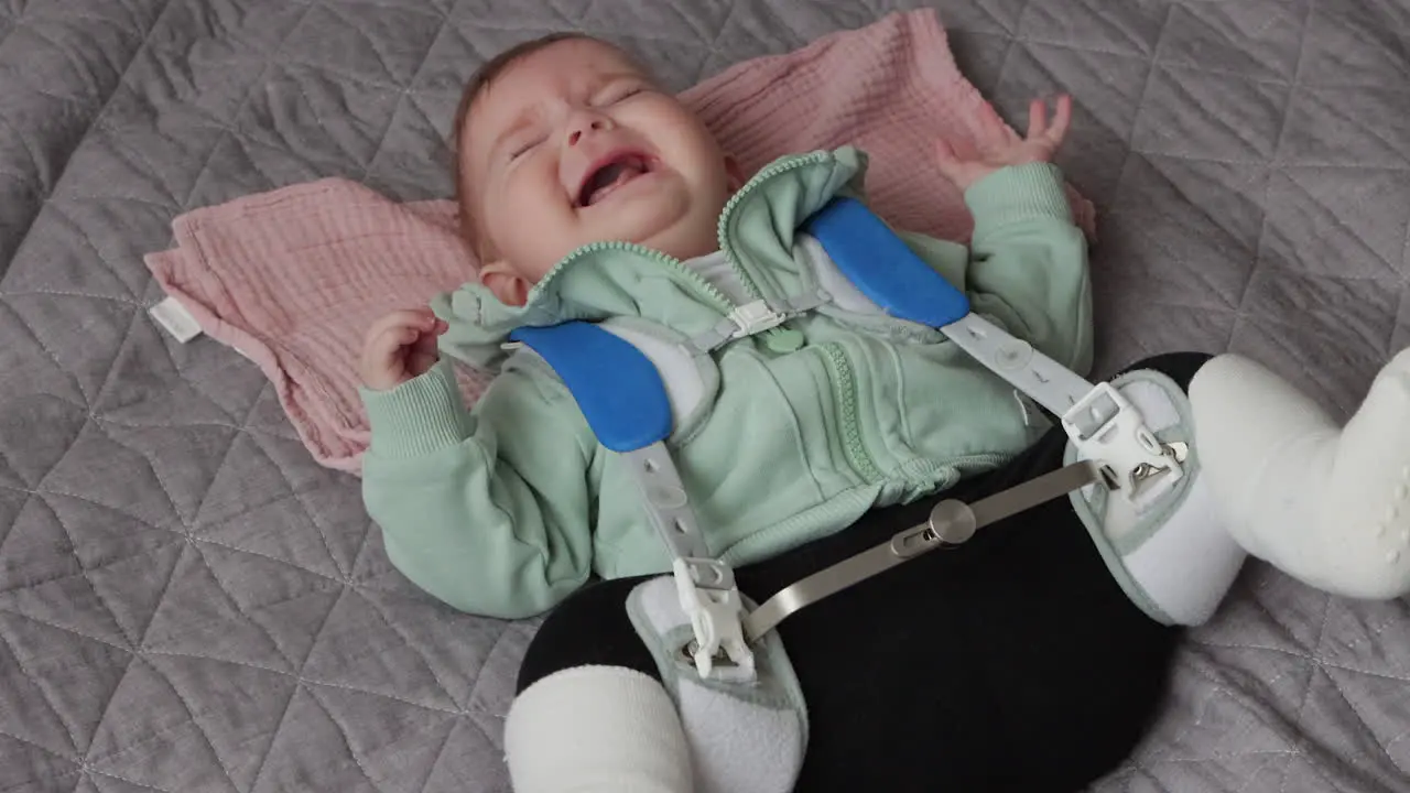 Baby girl in Pavlik Harness to correct Hip Dysplasia cries while lying on back