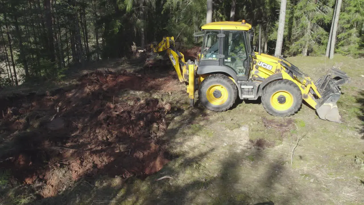 JCB tractor working in forest taking out tree roots and throwing them into pile