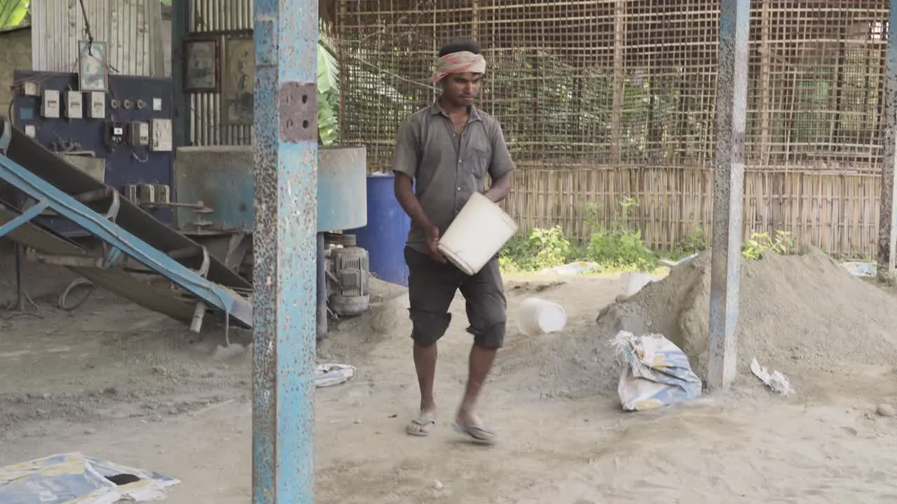 Indian worker in poor working conditions collecting clay sand in construction site building with a bucket