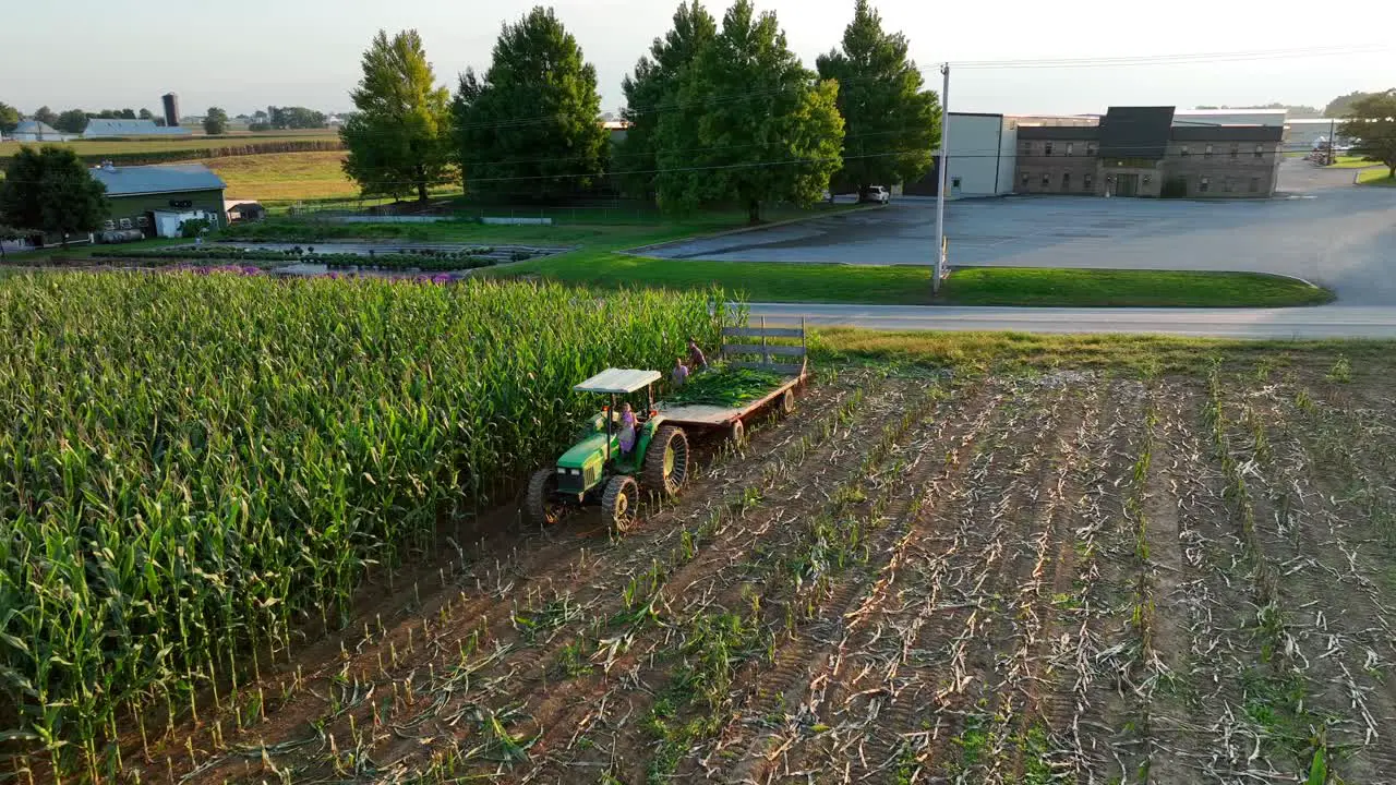 Children on John Deere tractor and wagon harvest corn in autumn aerial scene