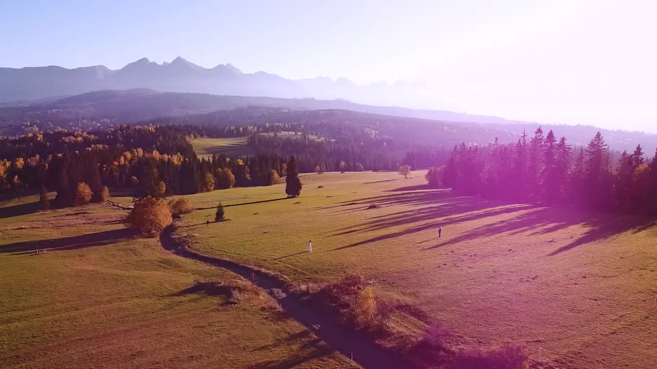 Aerial shot of young couple standing in front of huge mountains during sunset