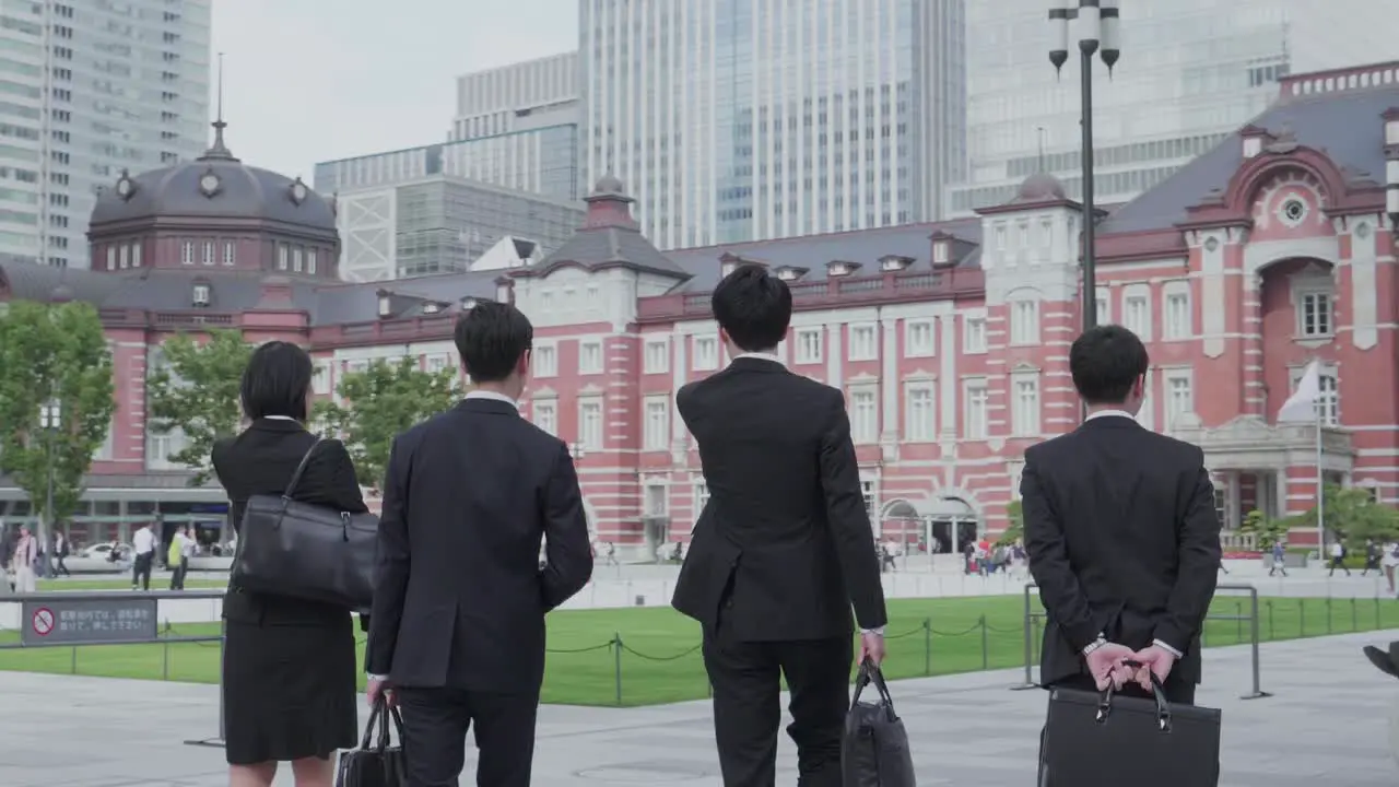 four young japanese business people in suits walking in front of Tokyo Station in Chiyoda Tokyo Japan on an overcast day