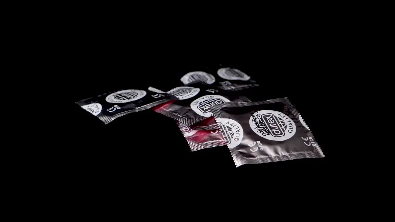 Silver condom packs are thrown on black surface in slow motion