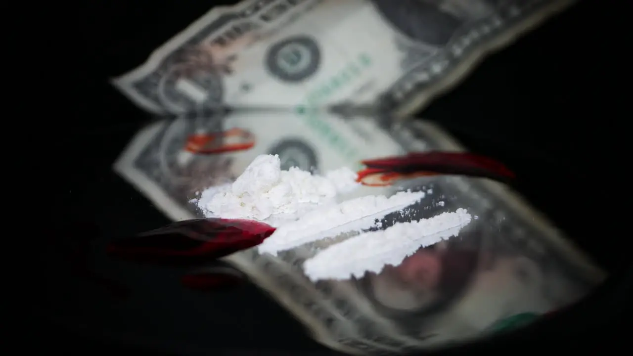 A Pile Of White Cocaine Powder With Blood Stain On Black Glass Turning Table Against Blurry Dollar Bill