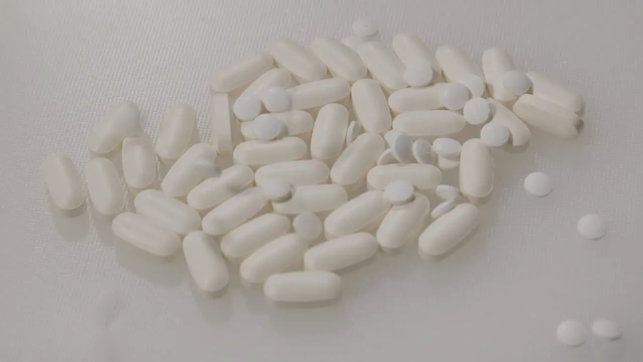 Small white pills falling on pile of pills on a white surface