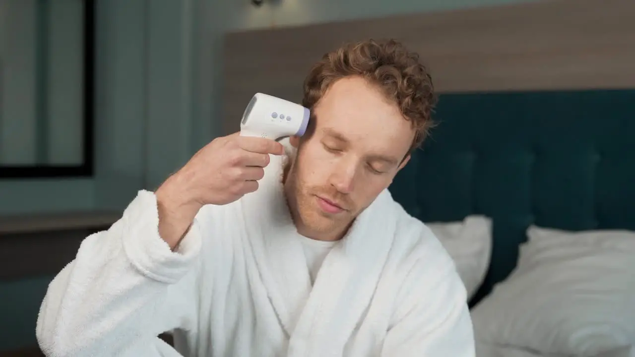 A young man in a bathrobe will measure his temperature with a non-contact thermometer