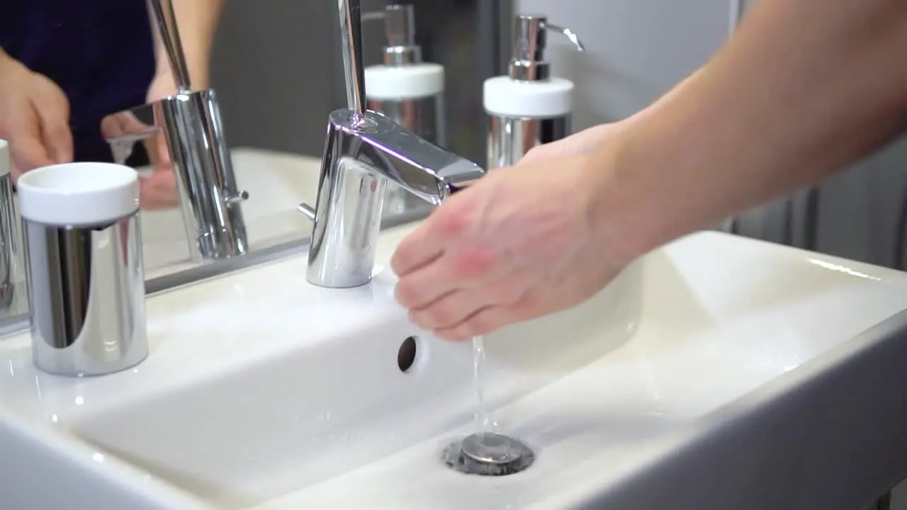 Slow-motion of white male washing hands with tab water in sterile bathroom