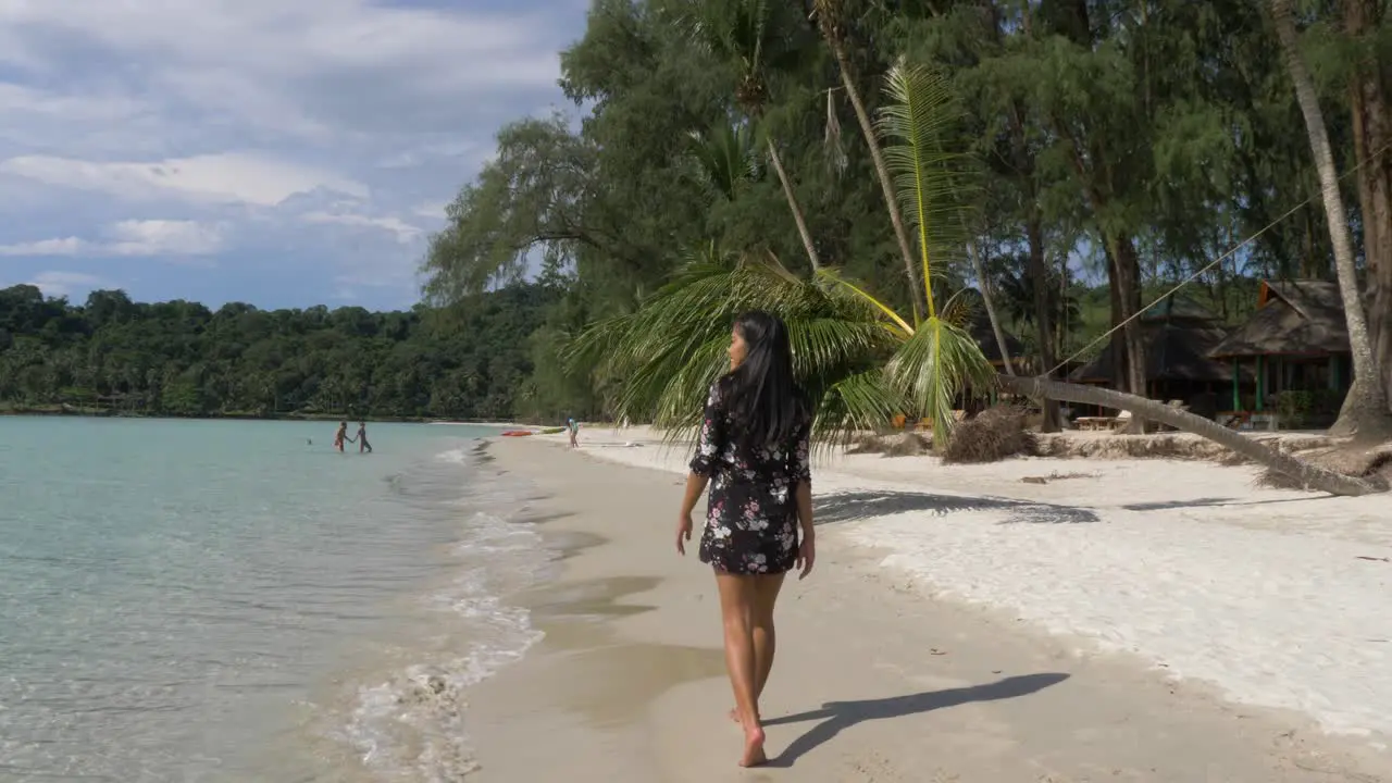 Asian Model in a short black flower dress walking on a tropical beach on the shoreline Slow Motion