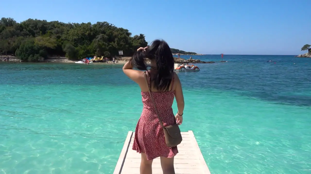 Girl in red summer dress walking on pier out towards turquoise ocean water in slow motion