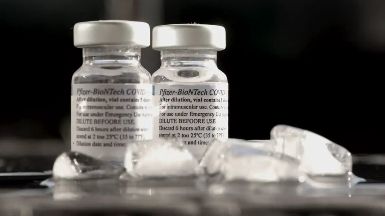 Two Bottles Of Covid Vaccine Made By Pfizer With Melting Ice Cubes On Foreground