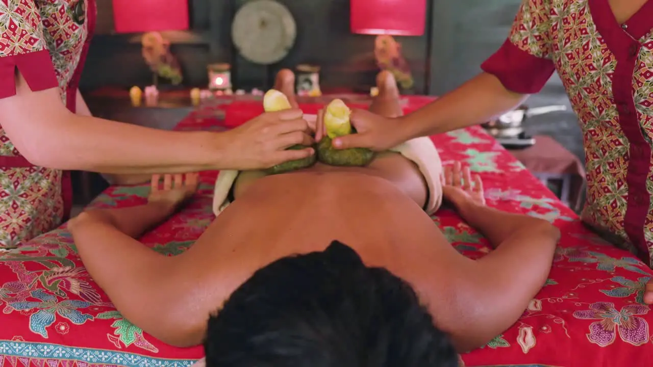 Two female spa therapists using herbal compresses to relieve tension from the back of a woman enjoying an Ayurvedic spa treatment