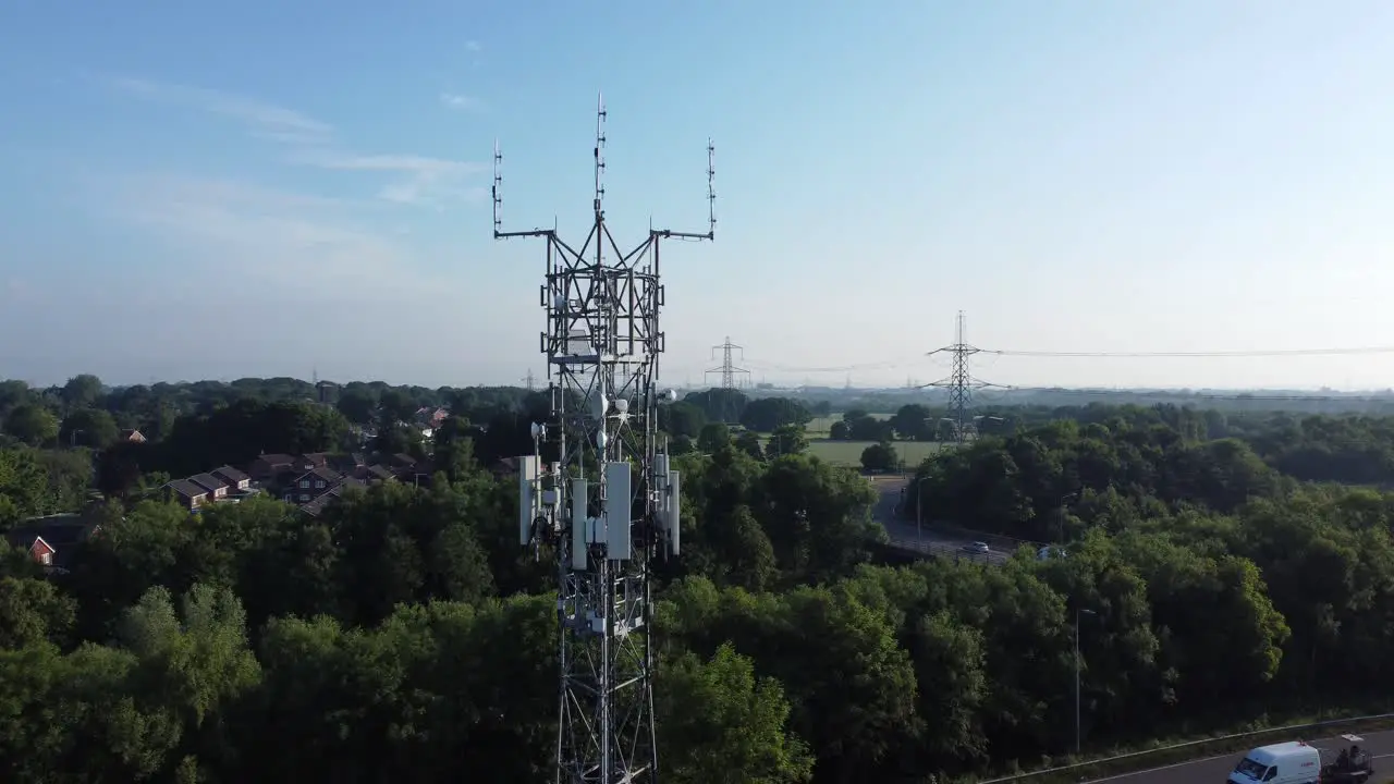 5G broadcasting tower antenna in British countryside woodland with vehicles travelling on highway background rising aerial view