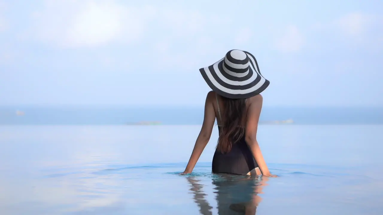 Sexy woman with hat in black One-Piece swimwear walking into calm sea