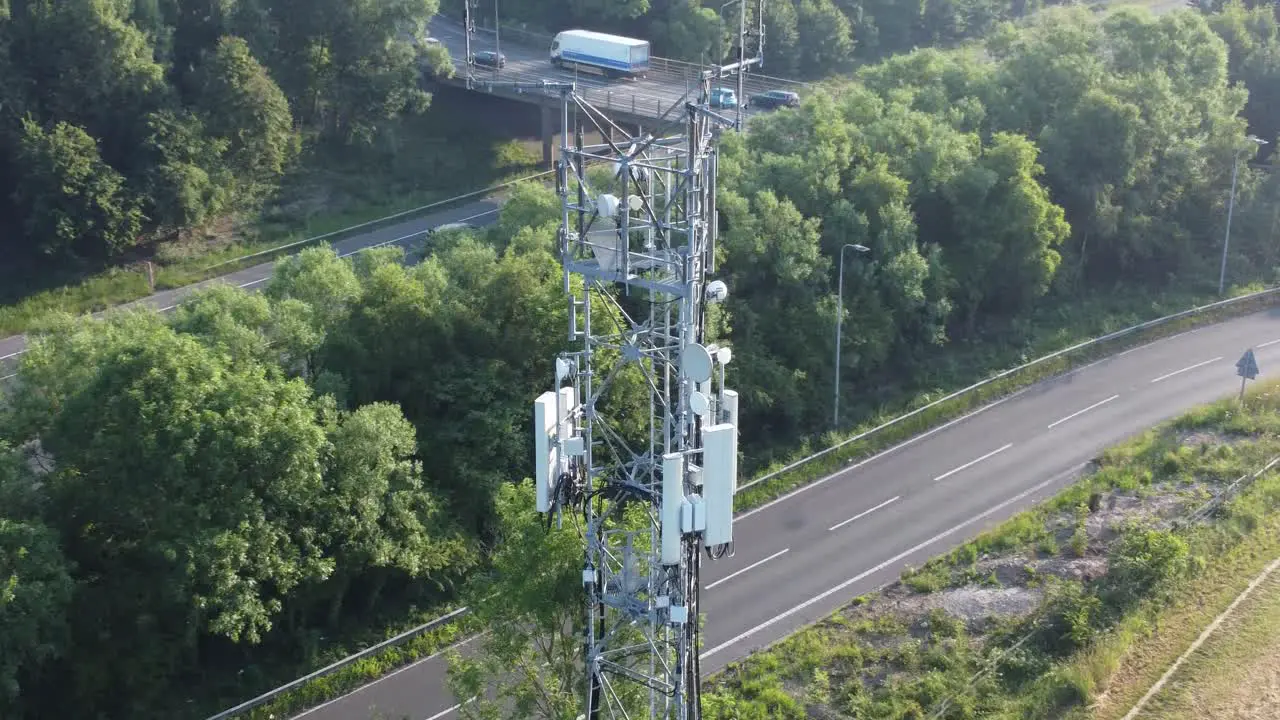 5G communication tower antenna in British countryside with vehicles travelling on highway background aerial orbit left view