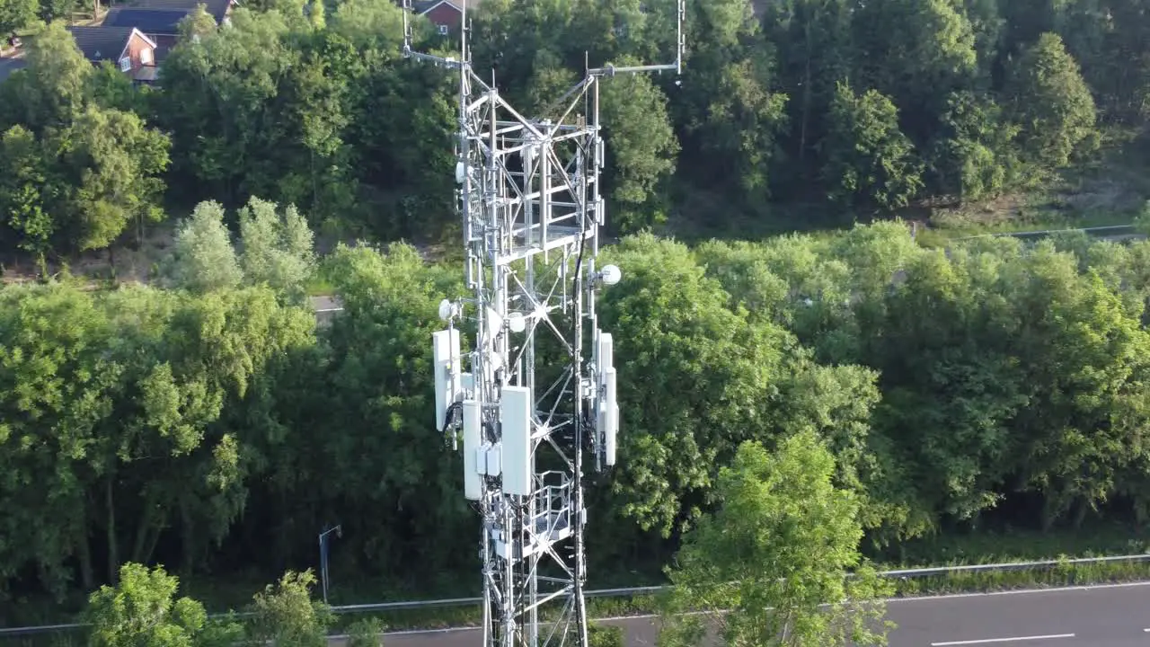 5G broadcasting tower antenna in British countryside with vehicles travelling between woodland background aerial orbit left