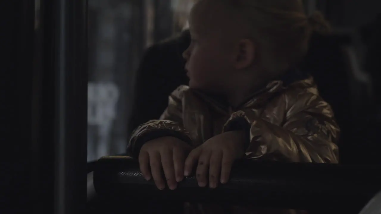 A baby girl in a golden jacket sitting in the bus on mothers lap