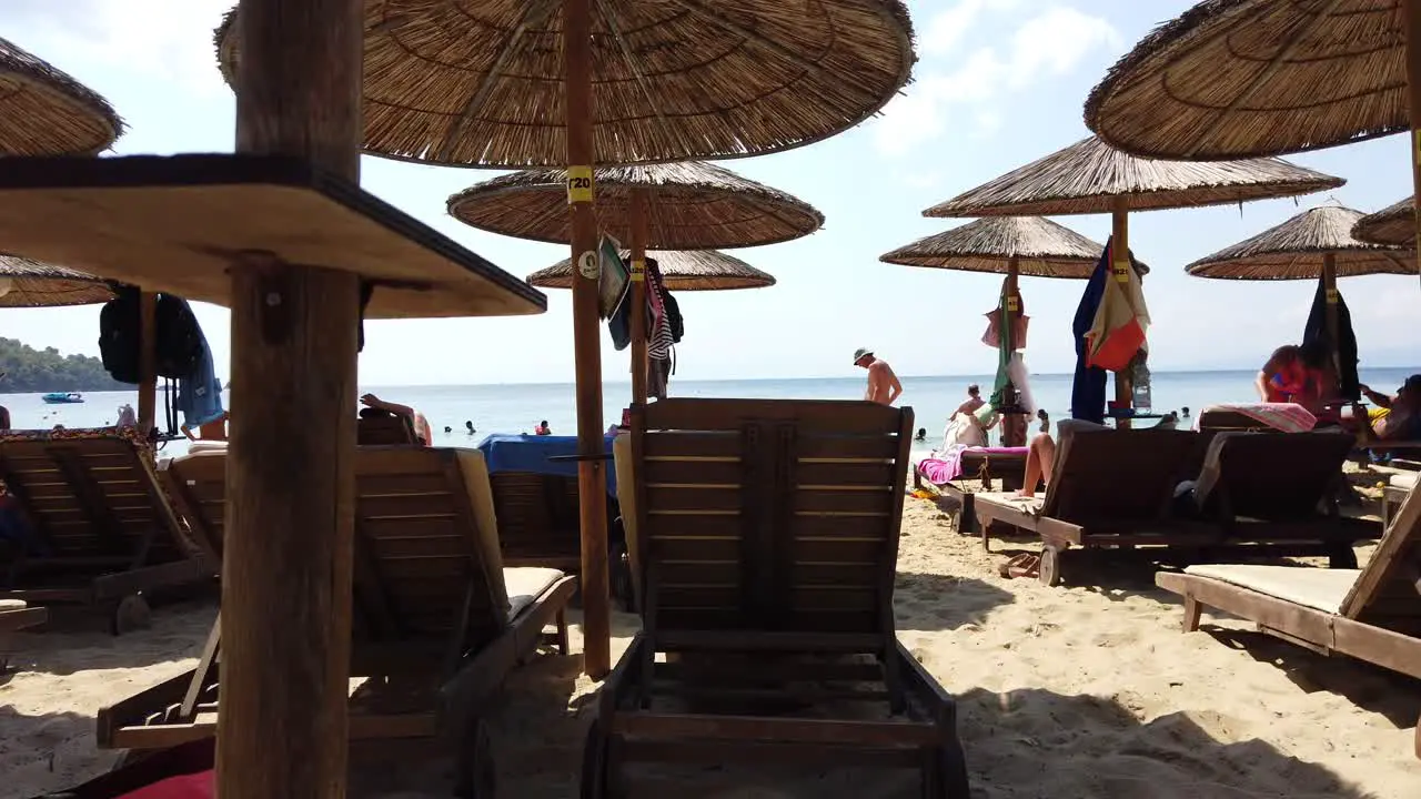 Panning Shot From A Tourist Taking Cover From The Hot Sun Under A Wooden Umbrealla