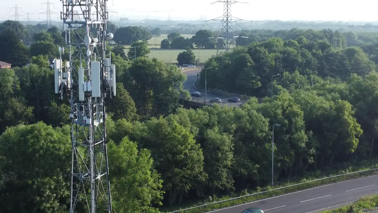 5G broadcasting tower antenna in British countryside with vehicles travelling on highway background aerial rising slow view