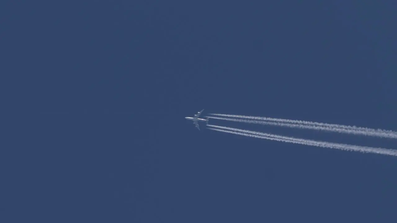 Four engine jet aircraft flies across a blue sky leaving a track bright white contrails behind