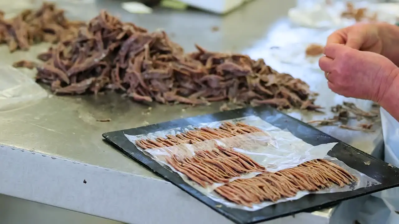 Worker tears rips and shreds dry pieces of shellfish placing onto tray for packaging