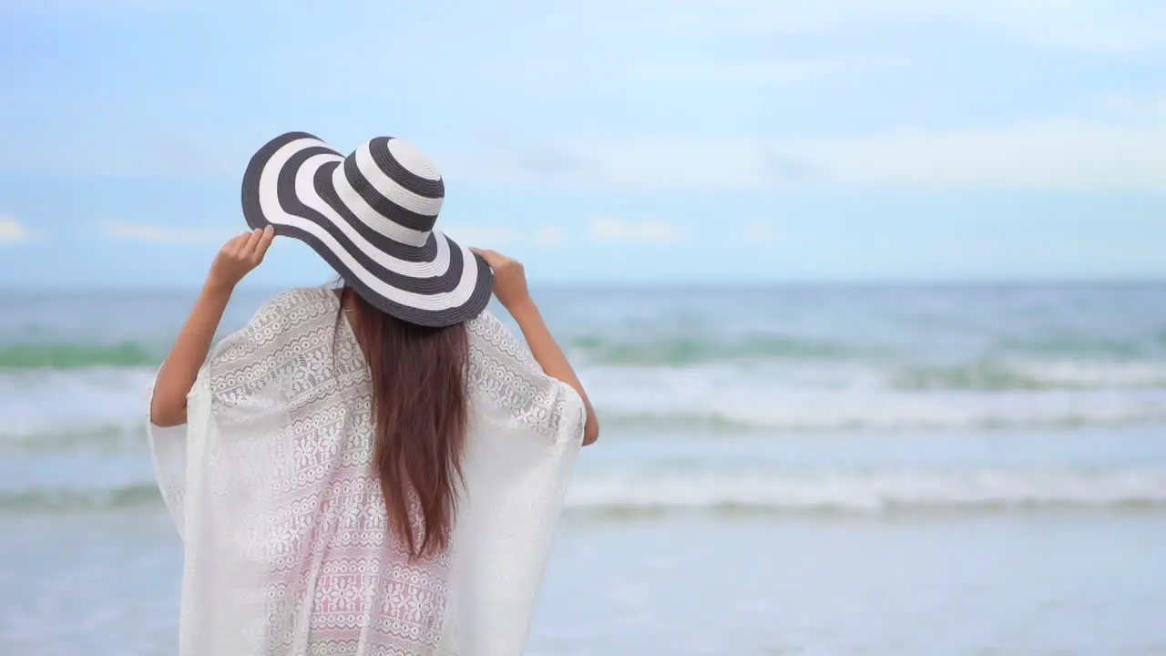 Asian Woman walking towards the sea on the beach and raising arms up vacation template back view