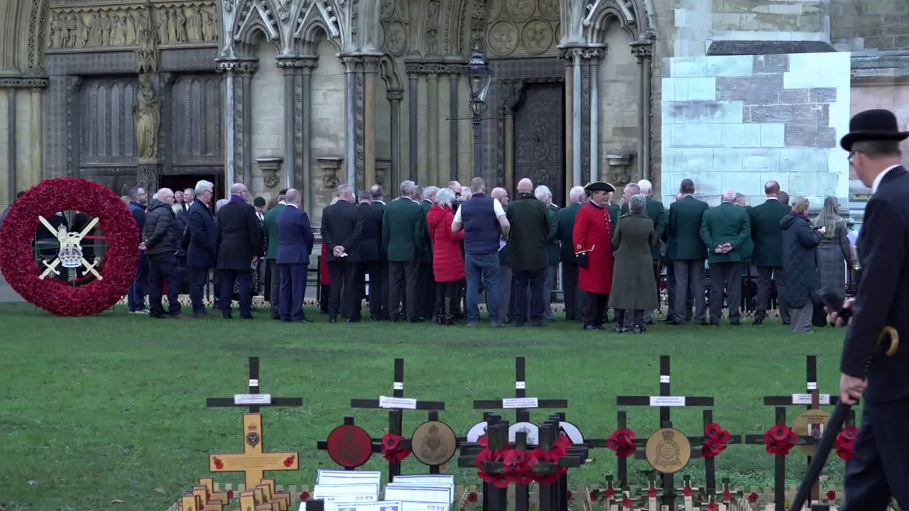 In slow motion a man wearing a bowler hat walks past tiny wooden crosses and a large wreath made of red poppies on Armistice Day at the Garden of Remembrance outside Westminster Abbey