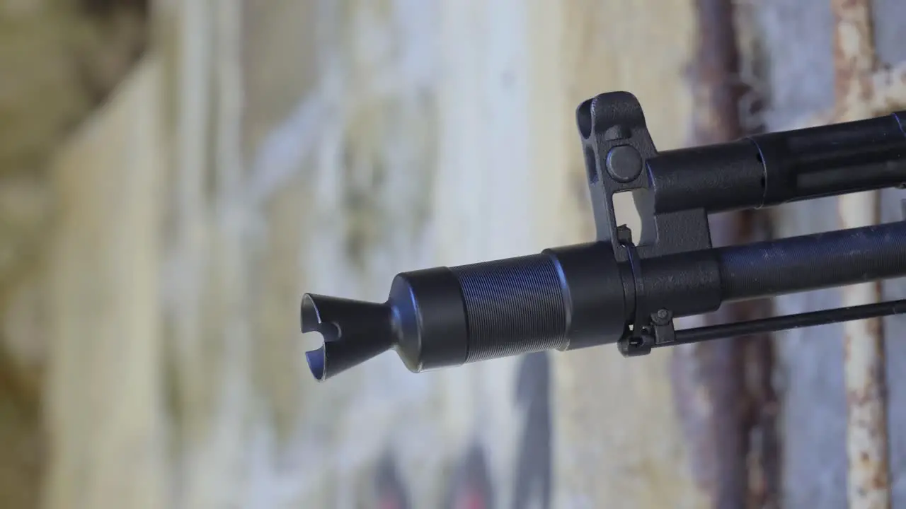 Close-up of the barrel of an AK automatic assault rifle as it enters frame against an old brick wall