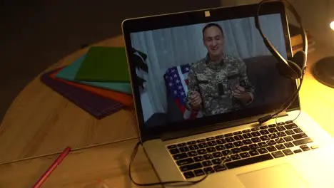 Brunette soldier man waving hand while making conference call on laptop indoors