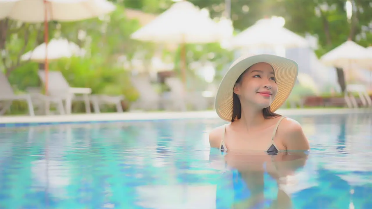 Dreamy scene with beautiful happy asian woman in swimming pool with floppy hat full frame slow motion