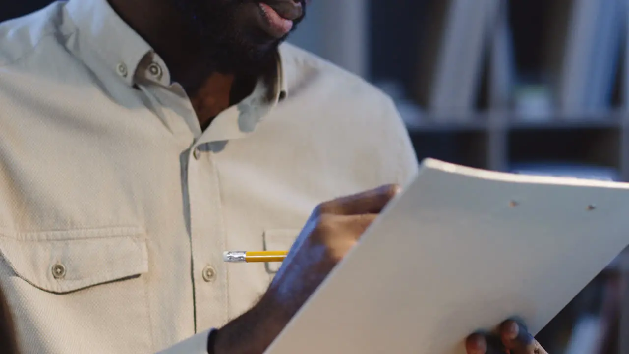 Close Up View Of Office Worker Sitting At Desk And Checking Some Documents With A Pencil In A Hand In The Office At Night