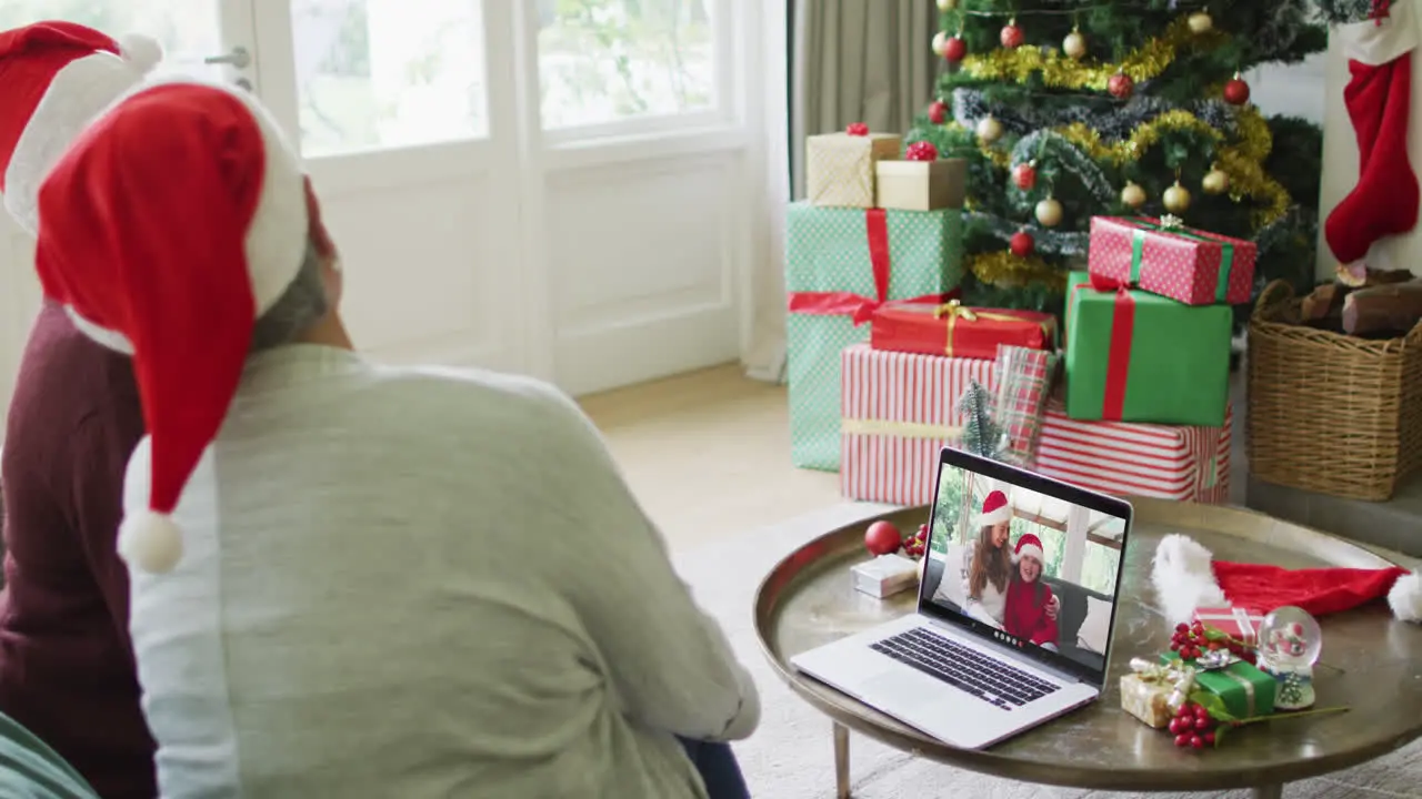 Diverse senior female friends using laptop for christmas video call with happy family on screen