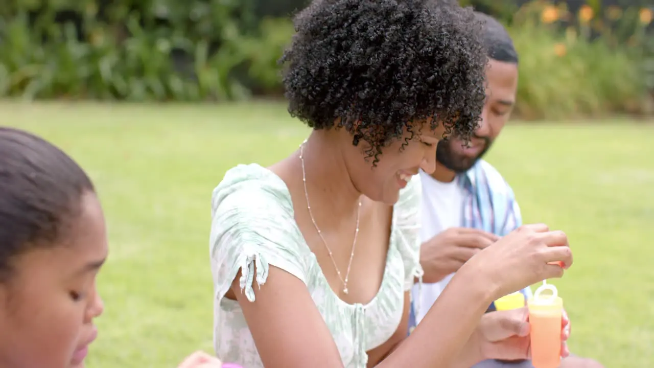 Happy african american parents and daughter blowing bubbles in garden slow motion