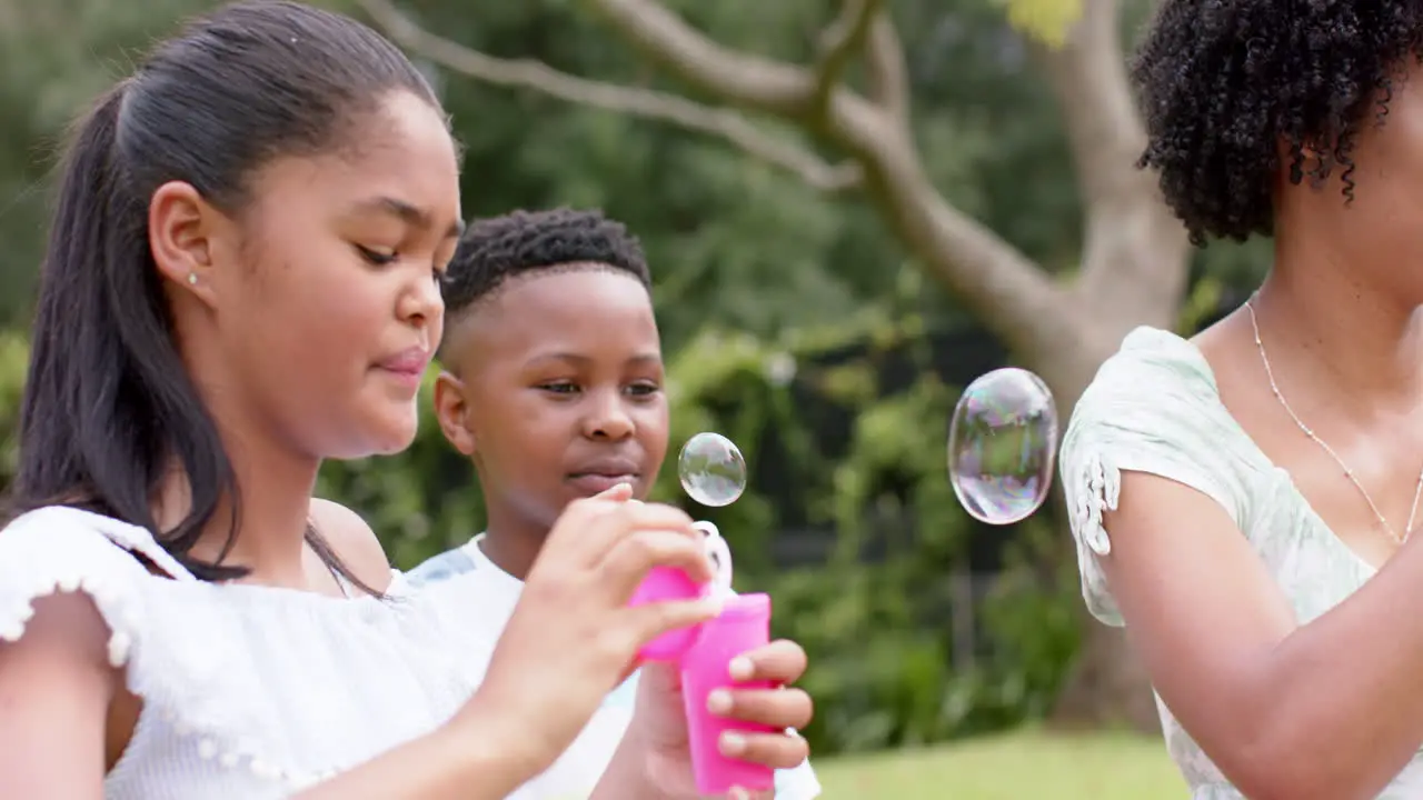 Happy african american mother daughter and son blowing bubbles in garden slow motion