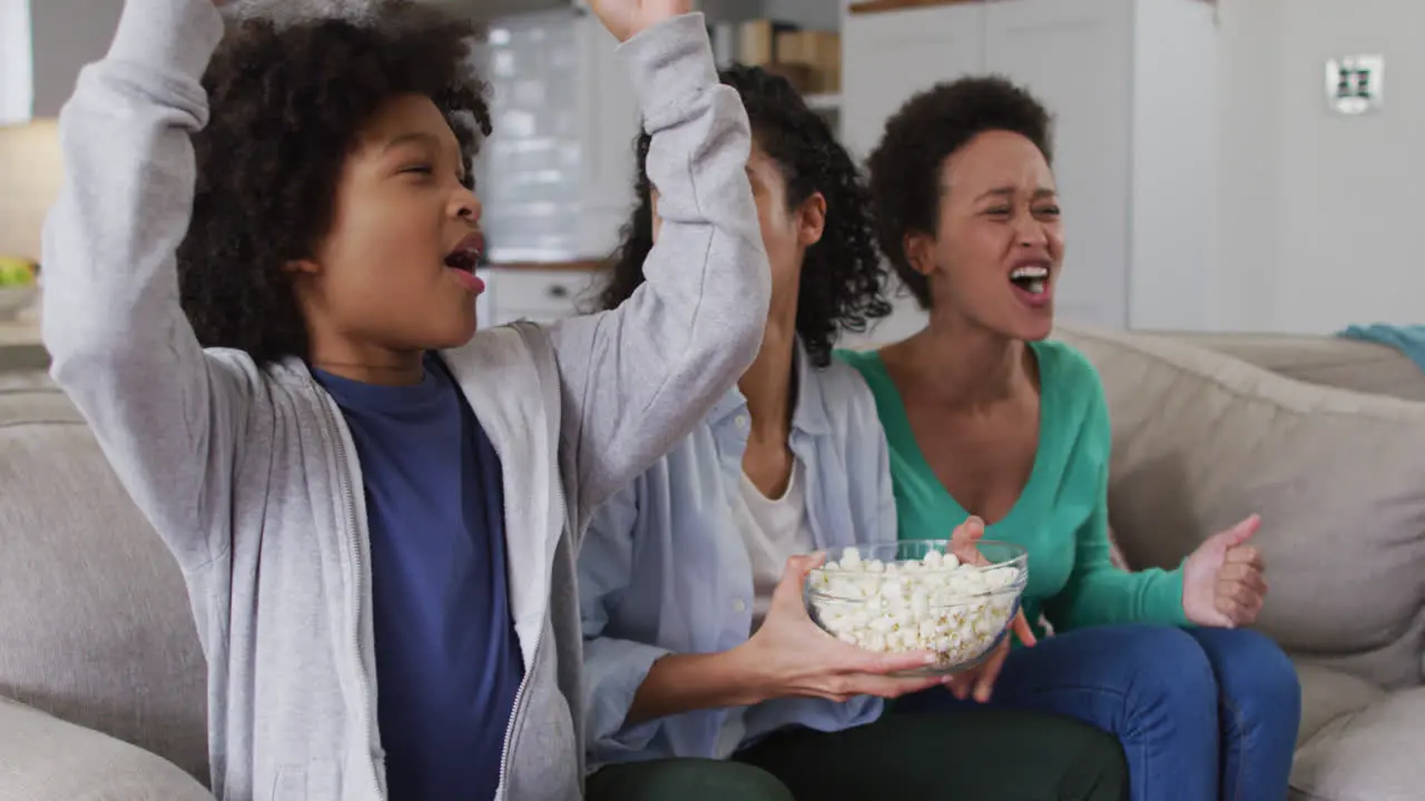 Mixed race lesbian couple and daughter watching tv eating popcorn high fiving