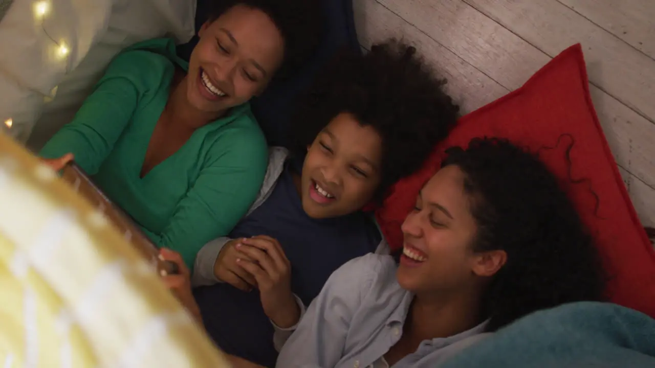 Mixed race lesbian couple and daughter using smartphone lying in bedroom camp