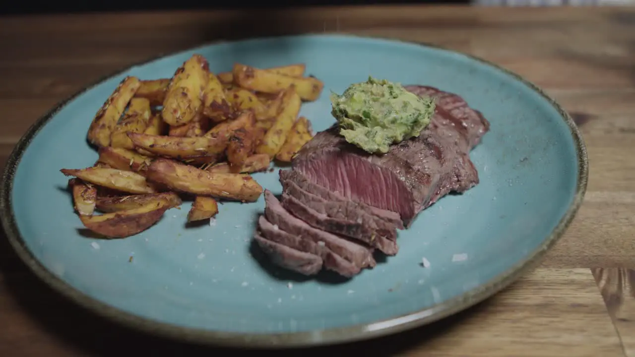 Chef adds salt to plate of meat slices with cafe paris butter and french fries