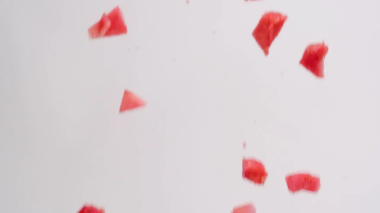 Pink juicy diced watermelon cube pieces raining down on white backdrop in slow motion